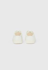 Λευκά αθλητικά παπούτσια με λείο δερμάτινο επάνω μέρος και μπεζ λεπτομέρεια στη φτέρνα. Διαθέτουν στρογγυλεμένη μυτούλα και ανθεκτική σόλα από καουτσούκ.