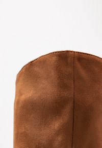 Bruna mocka ankelstövlar med en avsmalnande design, som har en slät struktur och en sydd söm längs den övre kanten.