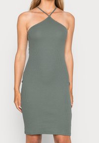 Ribbed, halterneck-mekko hillityssä vihreässä sävyssä. Istuva siluetti, jossa on sileä pinta ja ohuet hihnat, jotka risteävät selässä.