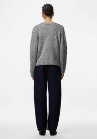 Pelēks adīts džemperis ar faktūru un ribinātu apakšmalu, kombinēts ar brīvām tumši zilām džinsu biksēm. Modelis attēlots no aizmugures.