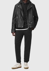 Svart läderbikerjacka över en svart hoodie, kombinerad med svarta joggers och vita sneakers med beige detaljer. Texturerade tygdetaljer synliga.