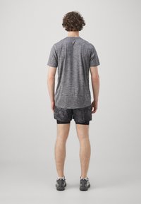T-shirt de sport gris à manches courtes avec une finition texturée, associé à un short noir à motifs ; le tout conçu pour être porté en activité sportive.