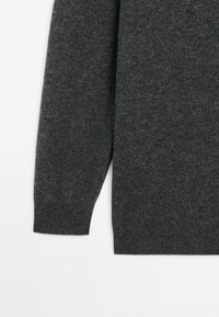 Pull gris foncé à manches longues, texture douce et coupe décontractée. Le tissu semble tricoté avec une surface lisse.