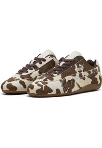 Tênis com estampa de vaca marrons e brancos, com textura de camurça, apresentando cadarços marrons e sola de borracha, com um logotipo branco na lateral.