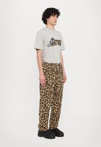 Gray t-shirt featuring a black and brown cat design, paired with loose-fitting, leopard-print pants in beige, brown, and black, and black shoes.