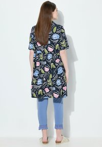 Marinblå tunika med blommönster i nyanser av rosa och blått, kombinerad med ljusblå caprisbyxor med spetsdetaljer, bärs med beige sk slipskor.