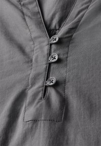 Camicia grigia con scollatura a V, quattro bottoni, e una consistenza morbida e liscia con dettagli di cucitura sottili attorno alla patta.