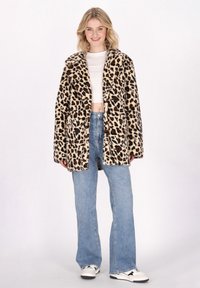 Leopardenmuster-Faux-Fur-Mantel mit langen Ärmeln, offener Vorderseite und lässiger Passform. Kombiniert mit einem weißen Crop-Top und hellblauen Jeans.