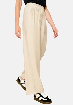 Light beige wide-leg pants made of a soft fabric, featuring a relaxed fit, front pleats, and an elastic waistband. Styled with black and white sneakers.