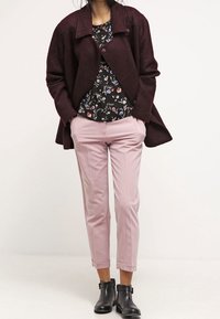 Cardigan bordeaux sopra una blusa nera floreale, abbinato a pantaloni a 3/4 rosa chiaro e stivali neri alla caviglia con fibbie.