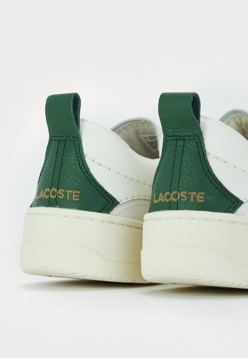 Baskets en cuir blanc avec des accents verts, des languettes arrière texturées et un logo doré à l'arrière. Semelle ronde et plate avec une finition lisse.