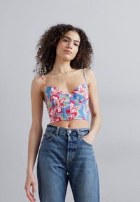 Kuttet, blomstermønstret topp som har blått stoff med store rosa og grønne blomster. Kombinert med høye, lys blå jeans.