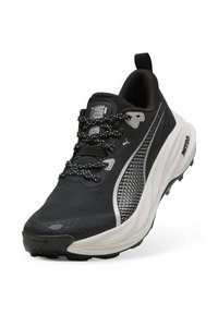 Zapatilla de running negra con parte superior de malla texturizada, acentos reflectantes y una suela gruesa blanca en contraste con un patrón de agarre.