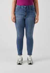 Modre skinny jeans iz denima z visokim pasom, z dvema sprednjima žepoma in šivanimi šivi. V kombinaciji z belimi in sivimi športnimi čevlji.