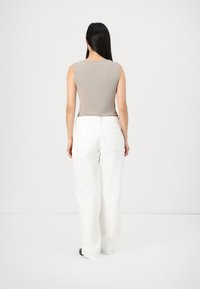 Beige bezrukávový top s ribovanou texturou, spárovaný s bílými kalhotami s vysokým pasem a širokými nohavicemi. Minimalistický design s čistou siluetou.