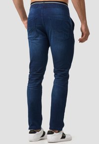 Men's blue denim jeans with a slim fit, elastic waistband, and two back pockets, showcasing a smooth texture and classic design.