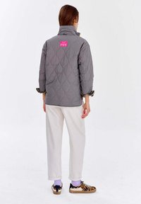 Prešívaná šedá bunda s vysokým golierom, na zadnej strane s ružovou visačkou. Nosí sa s krémovými nohavicami a teniskami s leopardím vzorom.