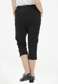 Pantalones cortos negros de material suave y elástico, con una cinturilla ancha de goma y dos bolsillos traseros. Combinados con calzado negro.