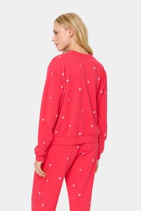 Piros pulóver és hozzáillő nadrág fehér szívmintával. Puha anyag, laza fazon, bordás mandzsetták és hajtás, látható varrási részletek.