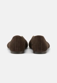 Ζευγάρι από σκούρα καφέ σουέντ φλατ παπούτσια, που φαίνονται από πίσω, με χαμηλές μαύρες σόλες και ορατή κάθετη ραφή σε κάθε τακούνι.