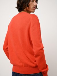 Ljusorange tröja i mjukt material, med rund halsringning, ribbade ärmslut och nederkant, samt en avspänd passform. Bakifrån, modell som bär jeans.