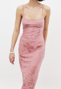 Roze, strak aansluitende jurk met dunne bandjes, voorzien van een bloempatroon dat op een gladde stof is geperst. Lange silhoutte met een elegante uitstraling.