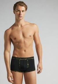 Boxer brevís negros con una cinturilla de camuflaje verde, que presentan un ajuste ceñido y material suave. Costuras notables a lo largo de las piernas y en la parte frontal.