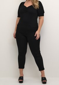 Haut ajusté noir avec un col en V et un détail froncé, associé à un pantalon noir slim. Chaussures dotées de mules noires ouvertes à l'avant.