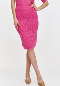 Dzianinowa spódnica ołówkowa w intensywnym różowym kolorze, z geometrycznym wzorem, prążkowanym paskiem w talii oraz dopasowanym krojem. Zestawiona z cielistymi szpilkami.