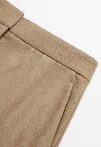 Tissu en mélange de laine couleur beige avec une texture douce. Présente un ourlet droit et des poches angulaires, mettant en avant un design épuré et structuré.