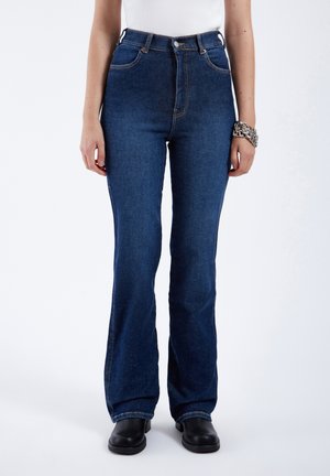 Dark blue flared jeans with a high waist design, made of denim. Features orange stitching, front pockets, and a zip fly with a button closure.