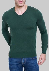 Sweater vert en v en tissu doux, design ajusté avec des manches longues et des poignets côtelés, associé à un jean en denim bleu.