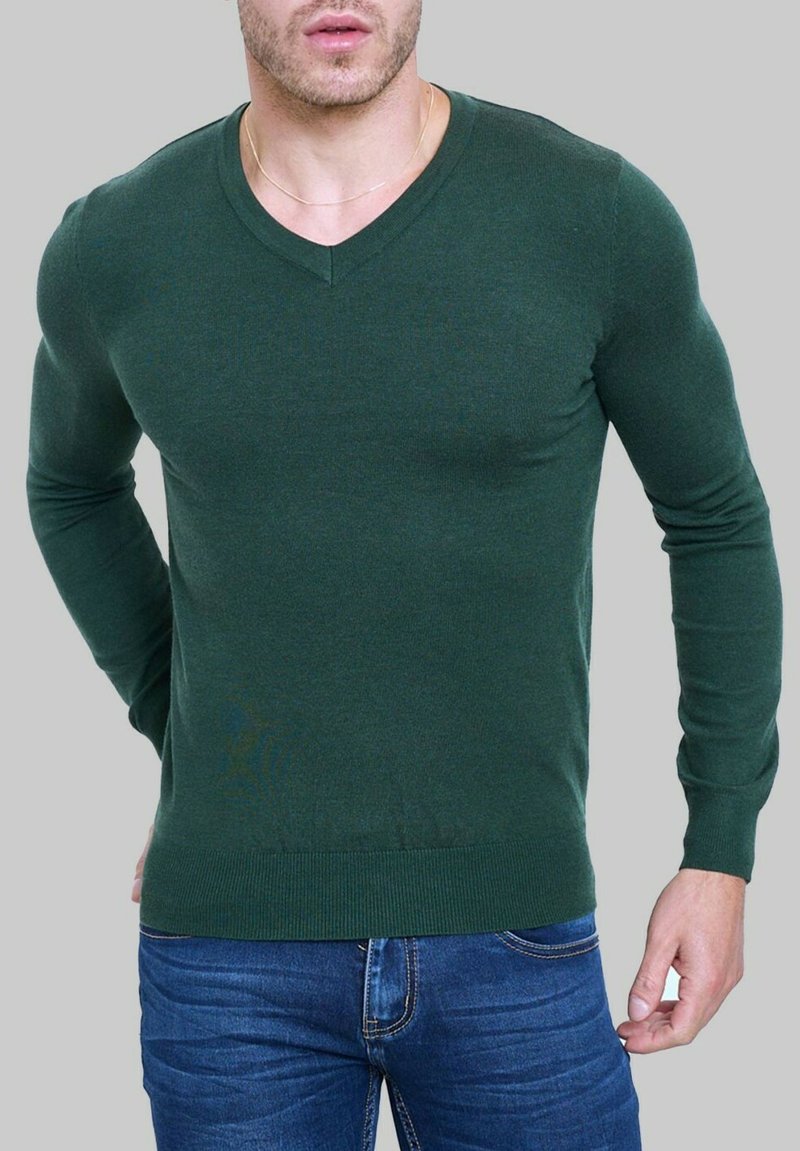 Sweater vert en v en tissu doux, design ajusté avec des manches longues et des poignets côtelés, associé à un jean en denim bleu.