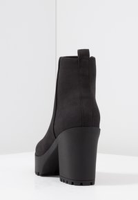 Stivale alla caviglia nero con tacco, dalla texture liscia, punta rotonda e suola piattaforma spessa. Presenta un bordo per facilitare l'indossamento.