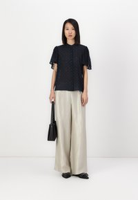 Blusa navy con maniche corte a volant e motivo testurizzato, abbinata a pantaloni a gamba larga di un pallido argento. Borsa nera e scarpe basse con dettagli.
