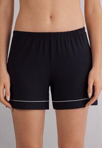 Černé bavlněné šortky mají elastický pas, bílé lemování a volný střih, což je činí vhodnými pro pohodlné a neformální nošení.