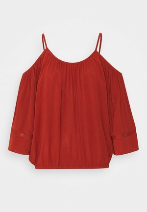 Blouse rouge à épaules dénudées avec fines bretelles, manches longues bouffantes, coupe ample, et détails subtils de tissu froncé.