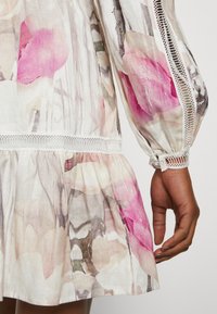 Kwiatowa sukienka z lekkiego materiału, z różowo-beżowymi wzorami, rozkloszowanym dołem i koronkowymi akcentami na rękawach dla dodatkowego efektu.