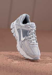 Sapatilha de corrida Nike Vapormax em cinza claro, com parte superior em malha, colarinho acolchoado e sola de borracha grossa com tecnologia de amortecimento a ar.