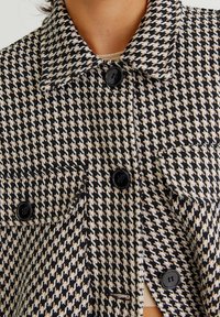 Zwart- en crèmekleurig jasje met ruitpatroon, kraag, zwarte knopen en zakken aan de voorkant. Geleverd in een getextureerde stof met een getailleerde pasvorm.