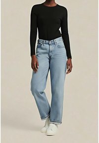 Mannequin portant un jean bleu clair taille haute à jambes droites, un haut noir ajusté à manches longues, et des baskets blanches sur un fond uni.