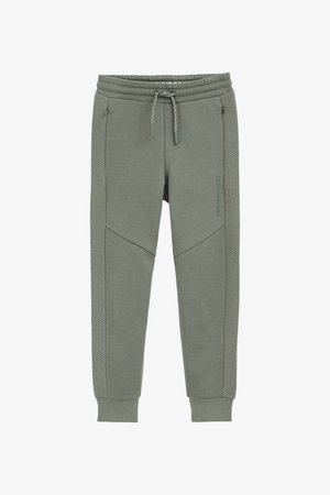 Zelene trenirke iz mehkega materiala, s rebrastimi robovi, elastičnim pasom in diagonalnimi teksturiranimi detajli ob straneh.