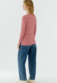 Rood- en witgestreept shirt met lange mouwen en een ronde hals, gecombineerd met blauwe, hooggetailleerde, wijd uitlopende jeans en beige schoenen.
