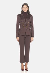 Blazer doppiopetto marrone con bottoni dorati, abbinato a pantaloni coordinati. Tessuto morbido, vestibilità su misura e design a gamba dritta.