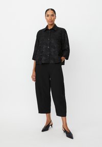 Sort mønstret jakke med knaplukning og trekvartærmer, parret med sorte brede bukser og sorte slip-on hæle.