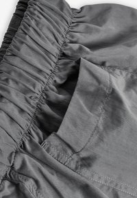Tissu gris avec une taille froncée texturée et une poche latérale. Les coutures sont visibles le long des bords, mettant en valeur le design décontracté.