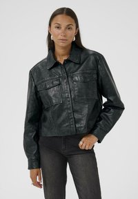 Kort zwart leren jasje met een kraag, twee voorzakken, knoopsluiting en een zachte textuur. gedragen met donkere jeans.