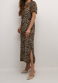 Robe imprimé léopard à manches courtes, taille cintrée et fentes latérales. Fabriquée en tissu léger, associée à des mules à talons beiges.