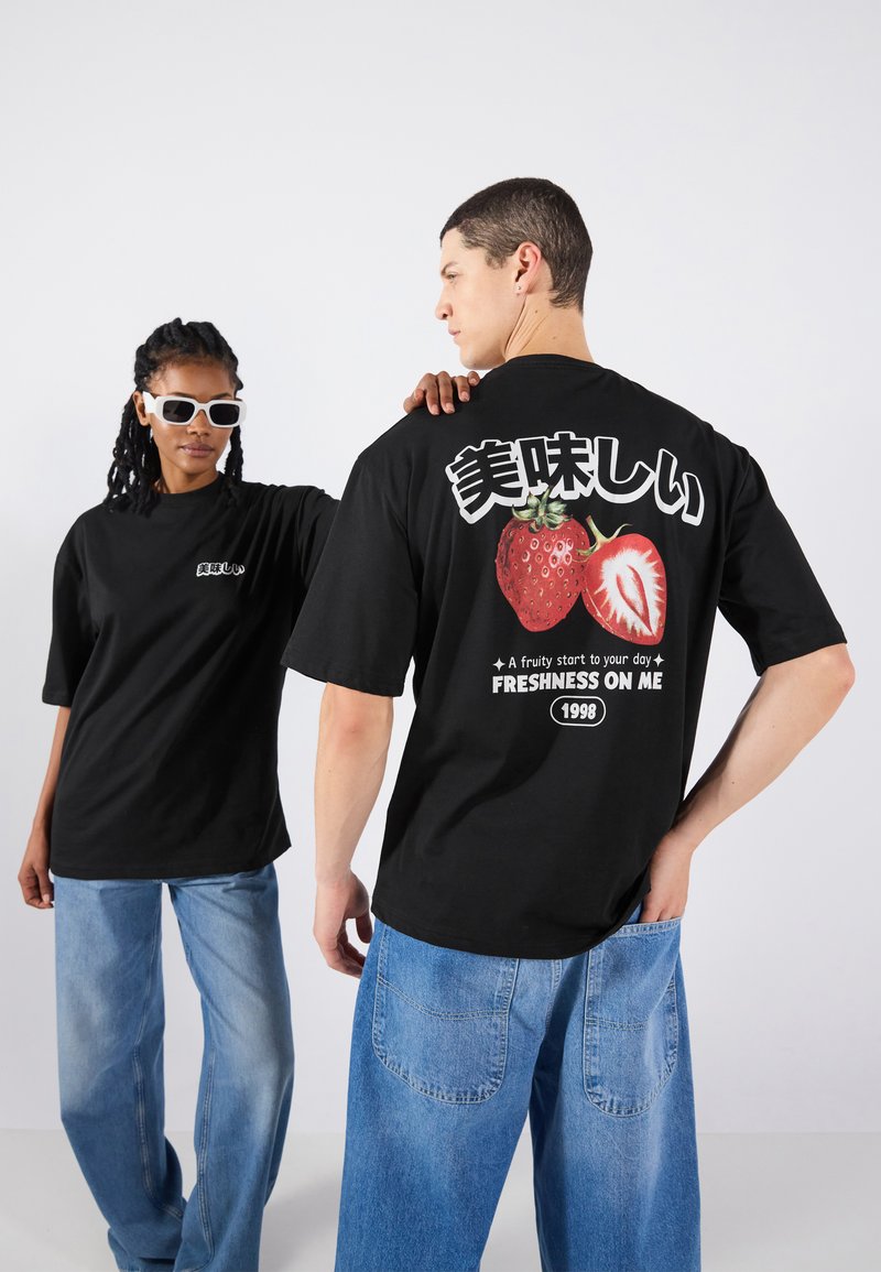 Black oversized t-shirts featuring strawberry graphics and Japanese text on the back. Model wears light blue loose-fitting jeans.