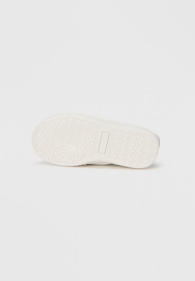 Λευκή σόλα παπουτσιού από καουτσούκ με υφή εξαγωνικού μοτίβου, που διαθέτει κυκλικό λογότυπο και ορθογώνια λωρίδα για επιπλέον πρόσφυση.